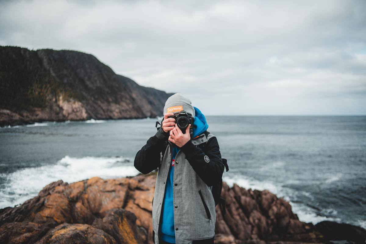 man holding camera by ocean dressed in warm clothes