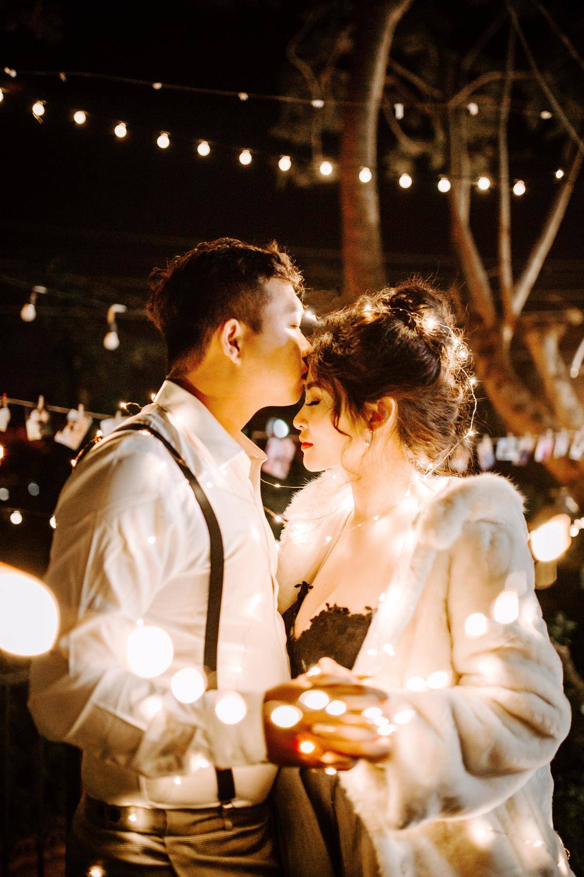 man kisses woman on the forehead while slow dancing with fairy lights