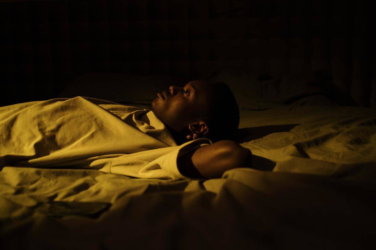 man thinking while laying in bed in yellow lighting