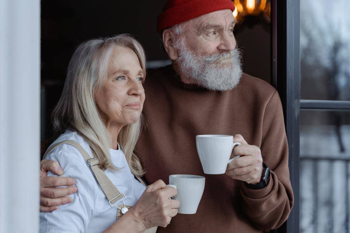 older couple hold coffees and look out the window