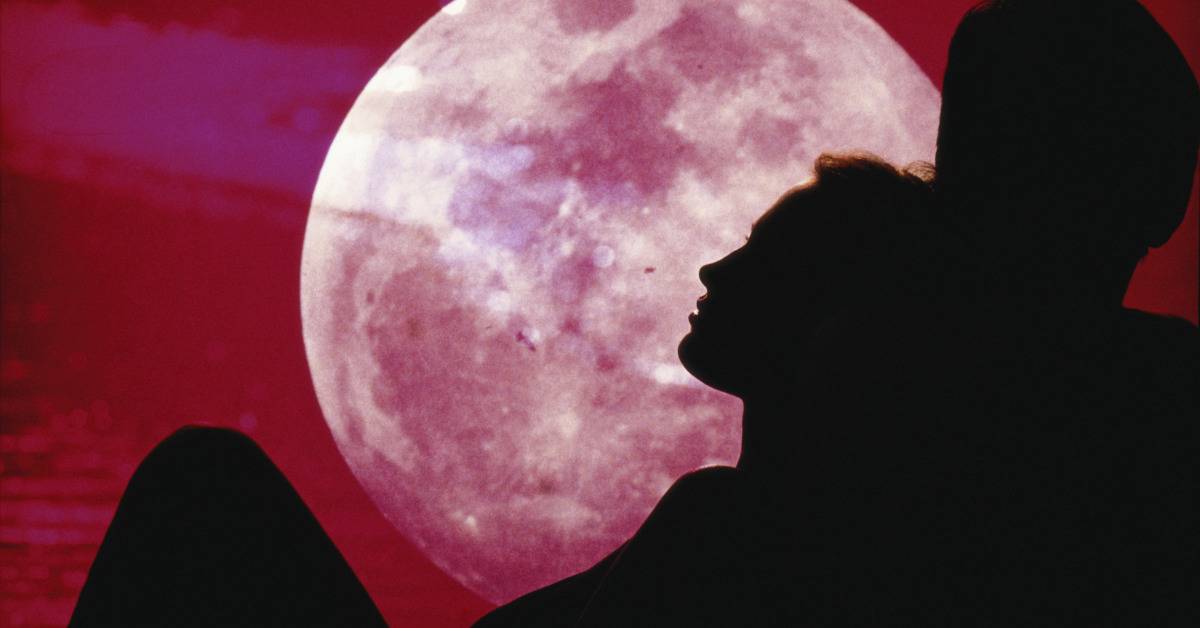 silhouette of couple laying down with pink moon in the background 