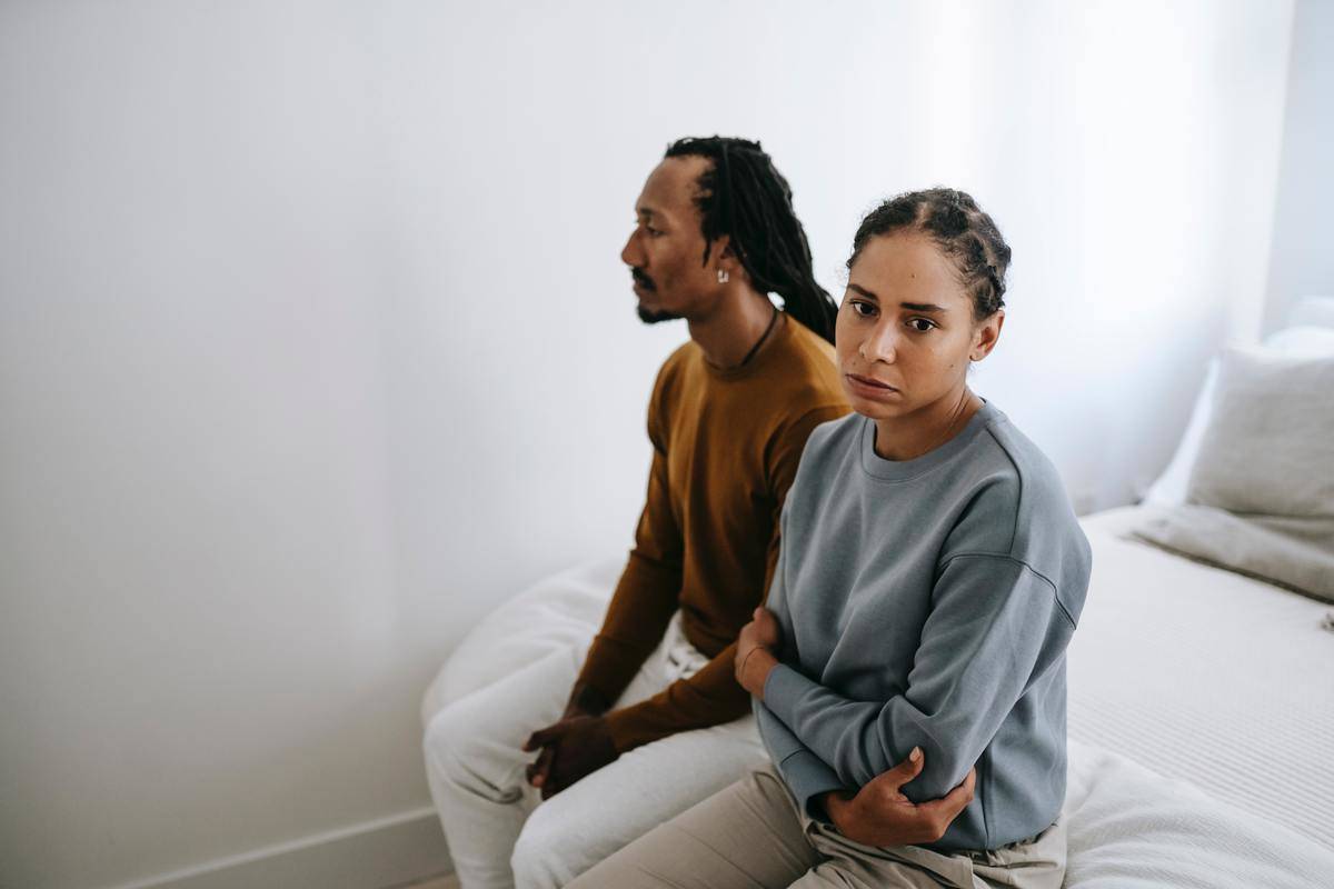 unhappy-black-couple-sitting-on-bed-togethe