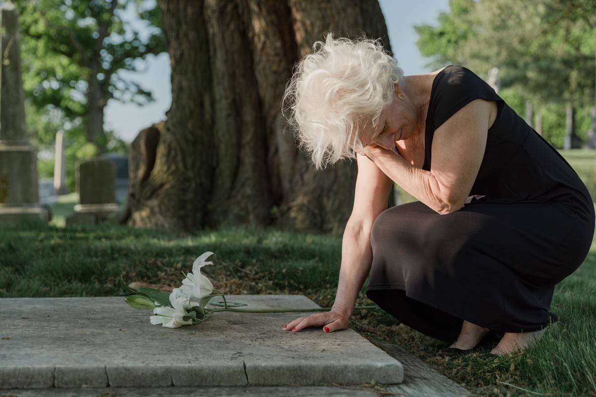 woman crying by tombstone in graveyard 