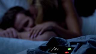 woman cuddlig up to sleeping man while wife calls phone