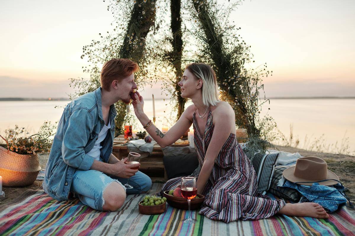 woman feeds man at picnic date by the water at sunset