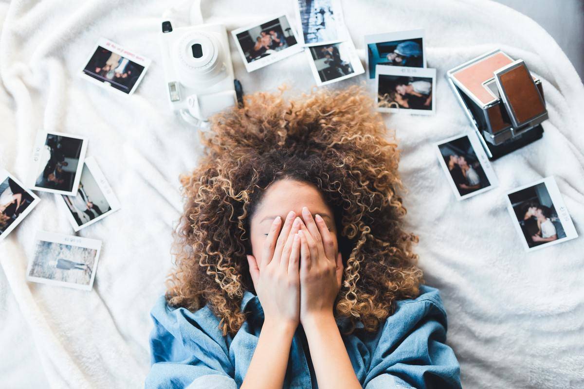 woman hides her face surrounded by poloraid pictures