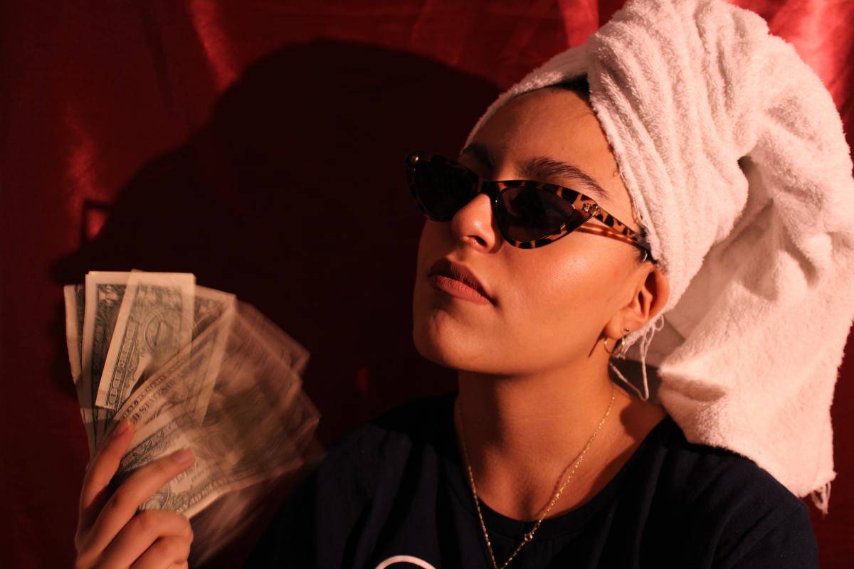 woman holding cash in her hands with sunglasses o and hair wrapped in a towel