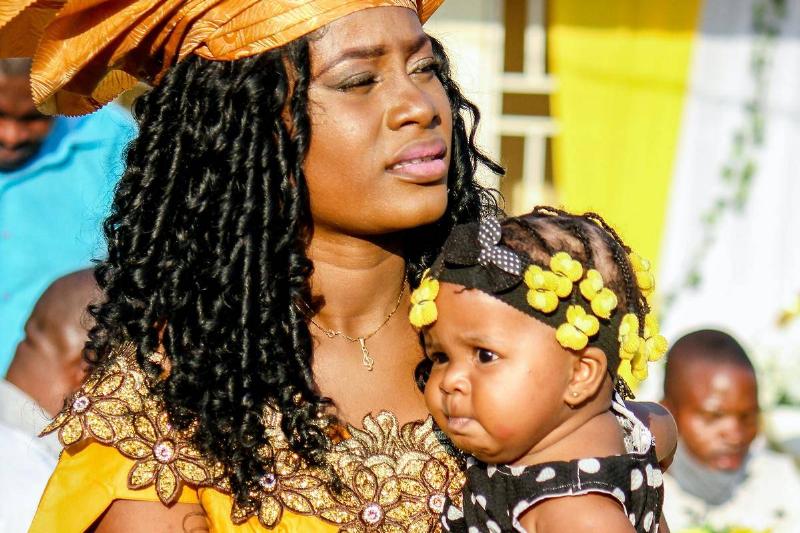 African woman in traditional clothes holds up baby