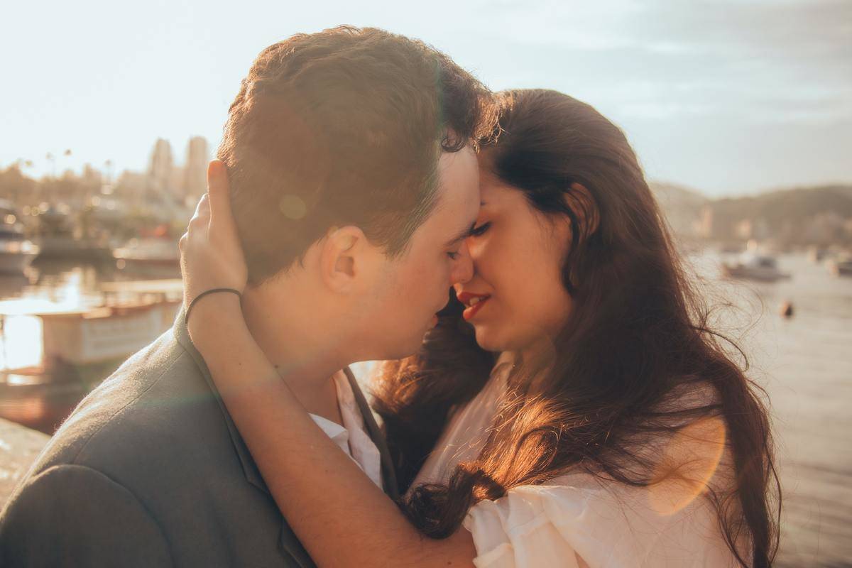 woman holds man's face close to kiss him by the sun