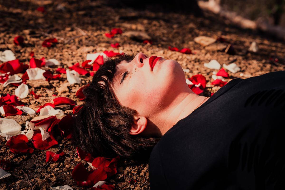 woman laying in red petals with eyes closed and red lipstick on
