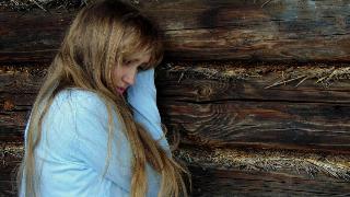 woman leaning against wood while crying