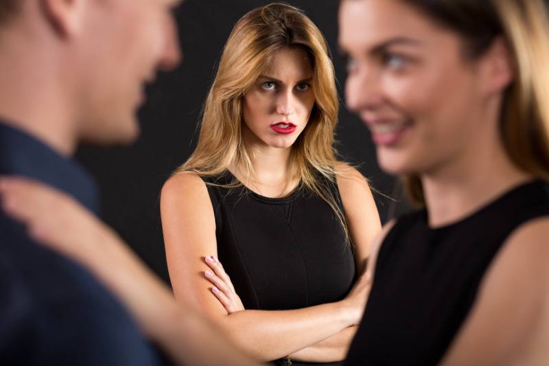 woman looking at couple talking with arms crossed