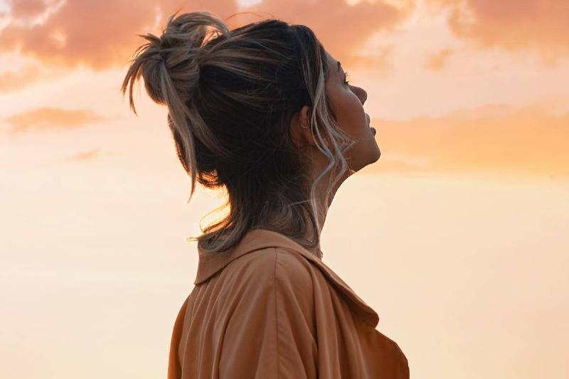 woman with hair bun looks up at sunset sky
