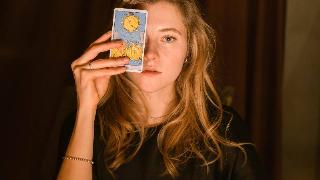 woman puts up tarot card to her eye by curtains