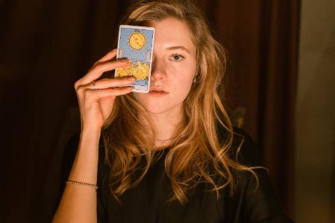woman puts up tarot card to her eye by curtains