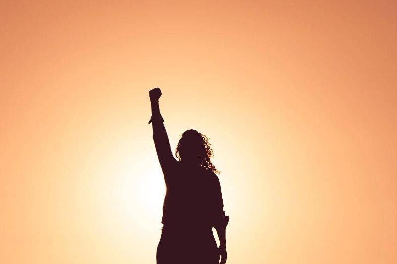 woman putting her fist up in empowering pose by sunset