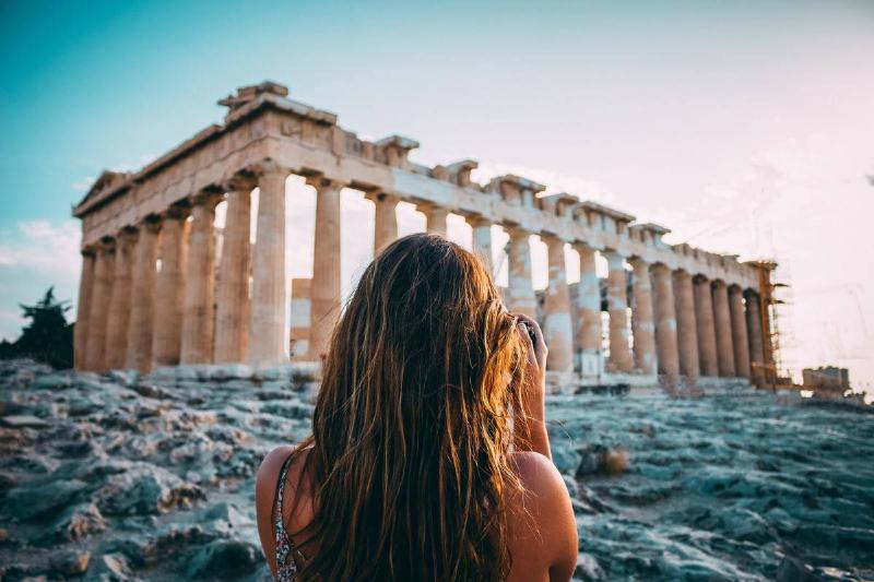 A woman standing in front of a Greek temple.