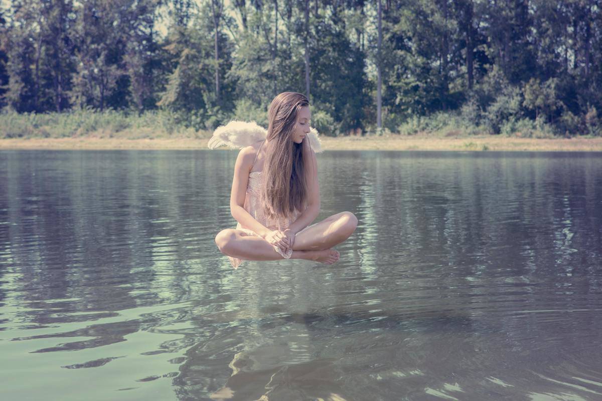 A woman levitating above a river, wearing angel wings.