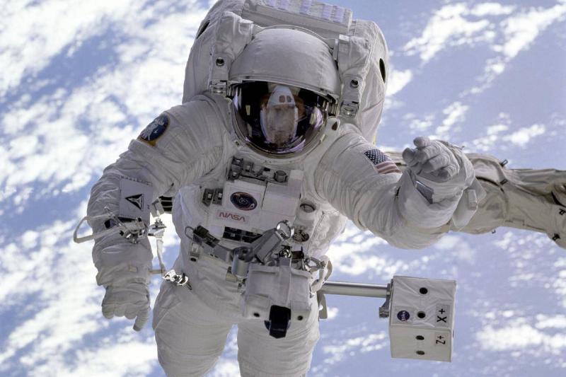 An astronaut in a white space outfit is floating in a cloudy blue sky.