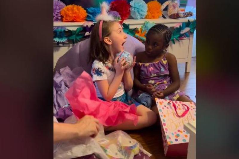 Two little girls sitting around birthday presents, one screaming in happiness.