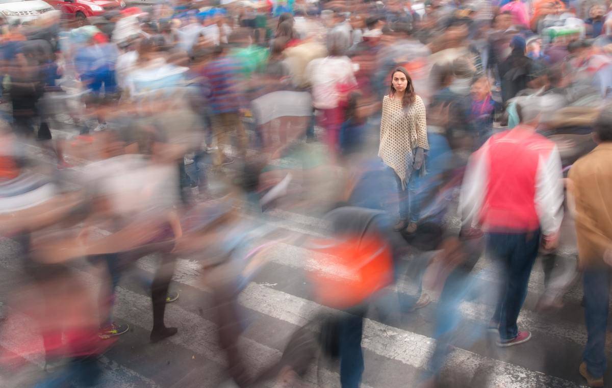 A woman walking on a street with blurred people scurrying past.