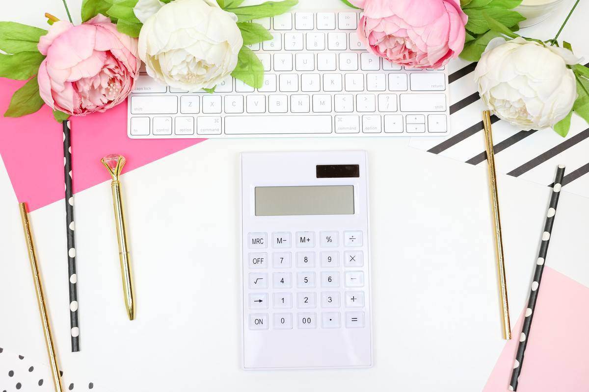 A white calculator sitting on a desk with pink flowers.