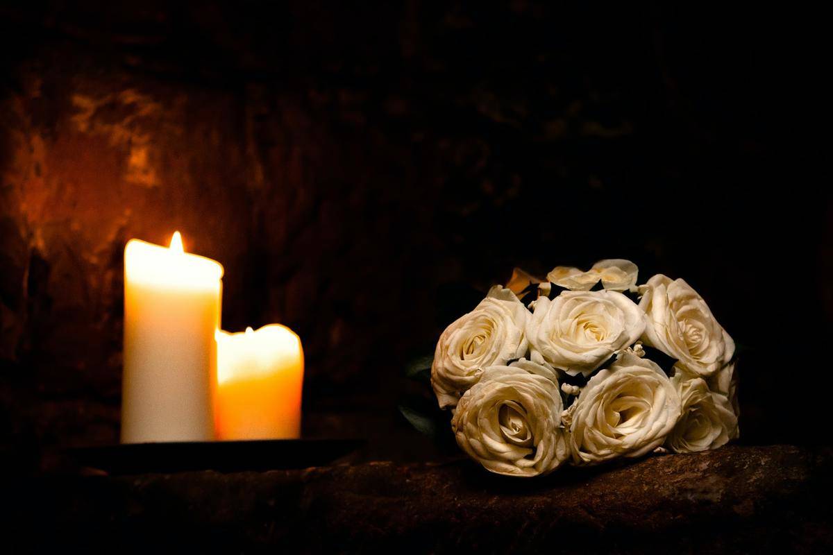 Two lit candles and a bouquet of white roses.