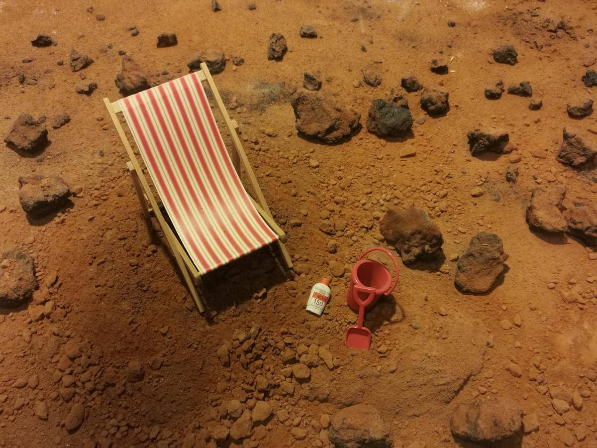 Ground covered in red sand with a single lawn chair and sand basket.