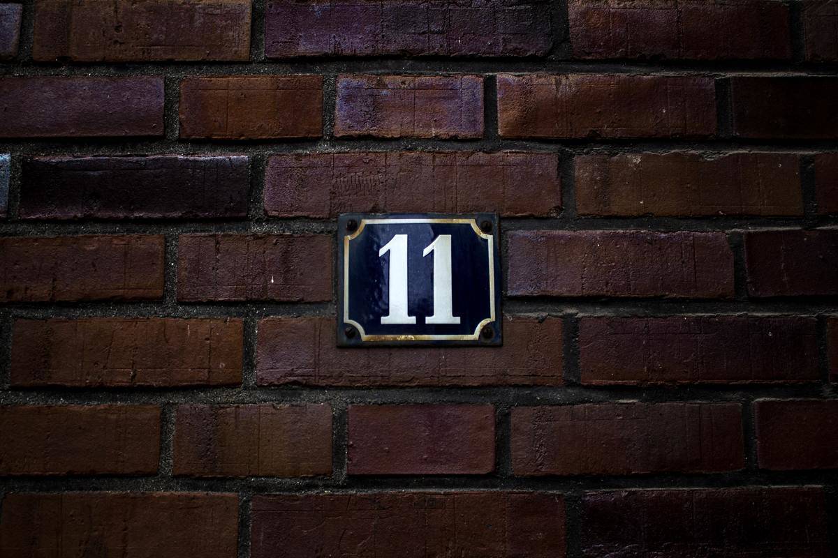 Number 11 hanging on a plaque on a brick wall.