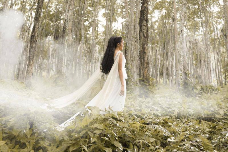 A woman in a white dress walking through a misty forest.