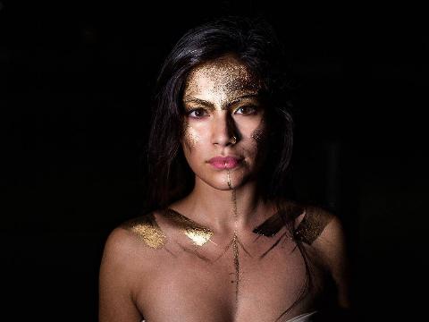 A woman with gold painted on her face and body.