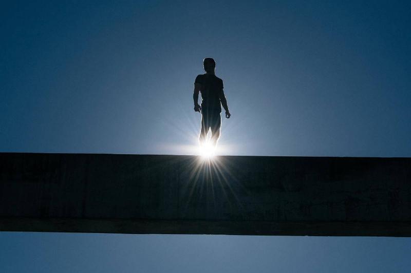 A silhouette of a man standing high on a bridge.