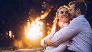 A man and woman sitting closely in a field at sunset.