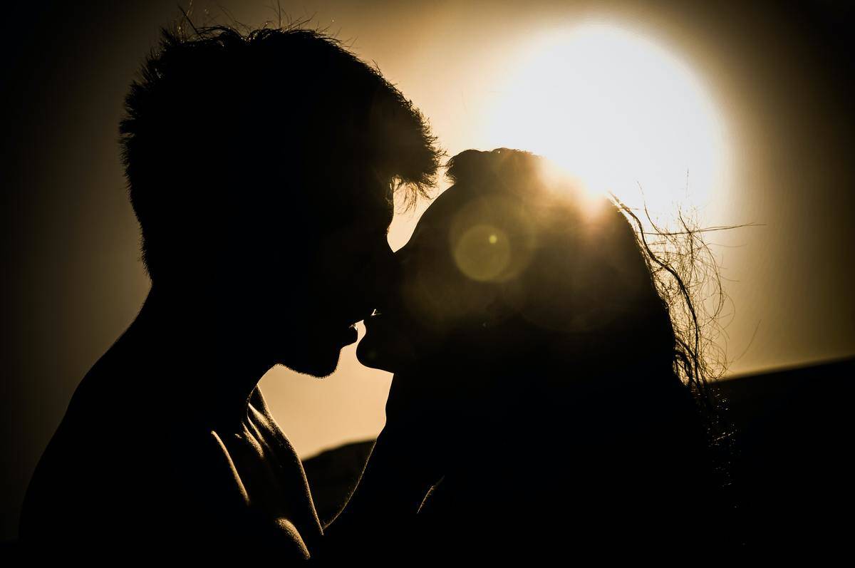 A silhouette of a man and woman kissing at sunset. 