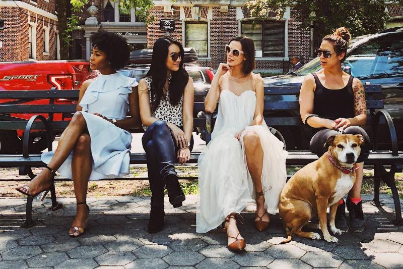 Four women and a dog sitting on a city park bench.