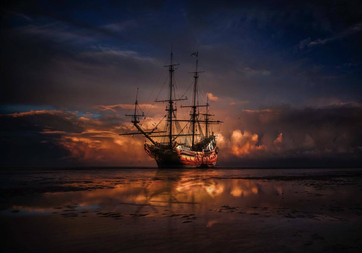 A pirate ship sailing in the water at sunset.