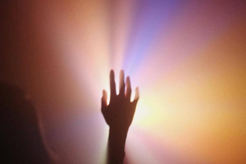 A hand reaching into colourful light.