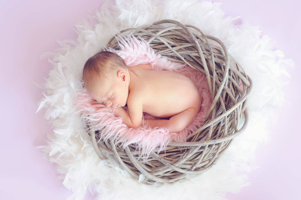 A newborn baby sleeping in a wooden basket. 
