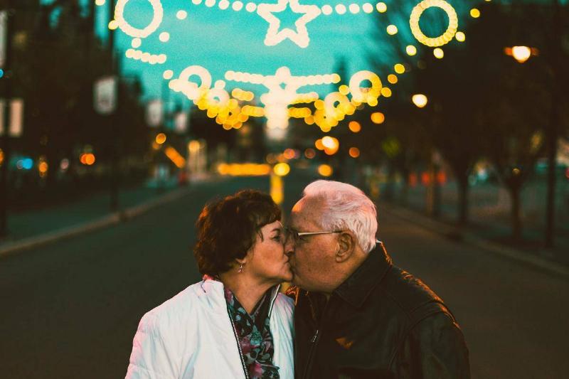 An elder couple kissing in front of street lights.