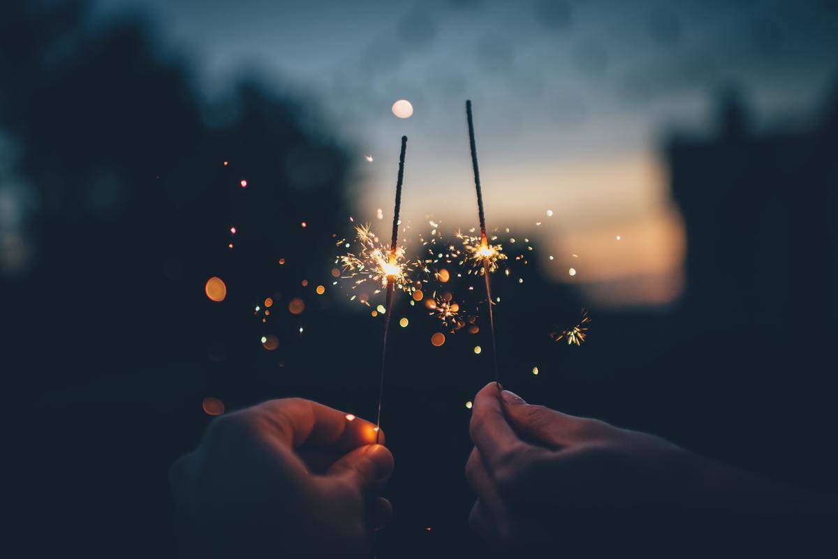 Two hands holding sparklers in night sky
