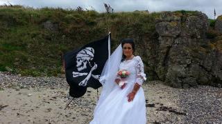 A woman wearing a wedding dress and standing beside a pirate flag.