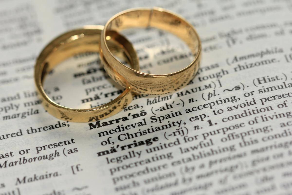 Two gold wedding rings lying on top of a dictionary that reads the word 