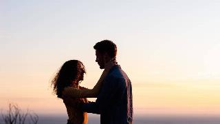 A young couple glaring into each other's eyes at sunset by the water.
