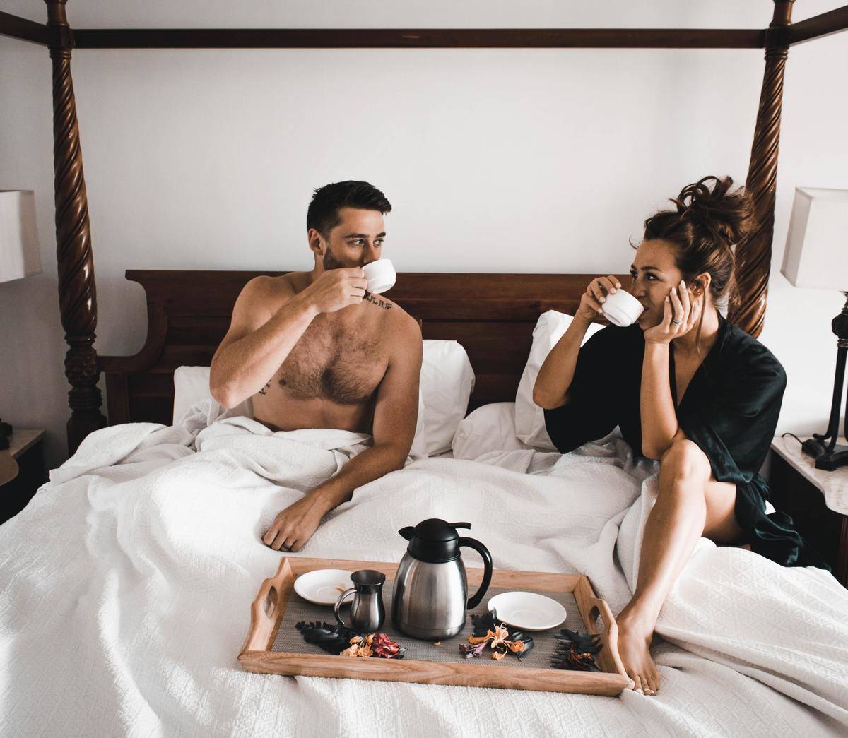 man and woman have breakfast in bed while looking at each other
