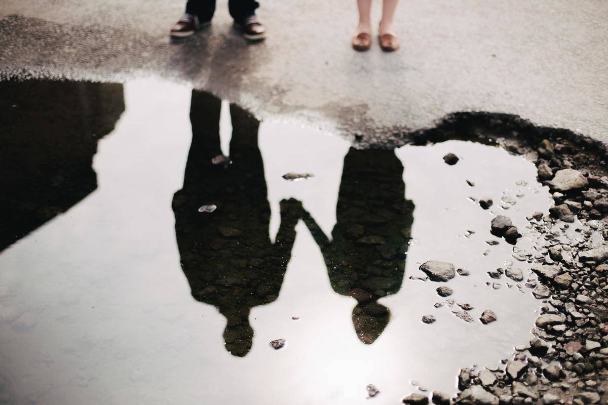 man and woman holding hands reflected in puddle