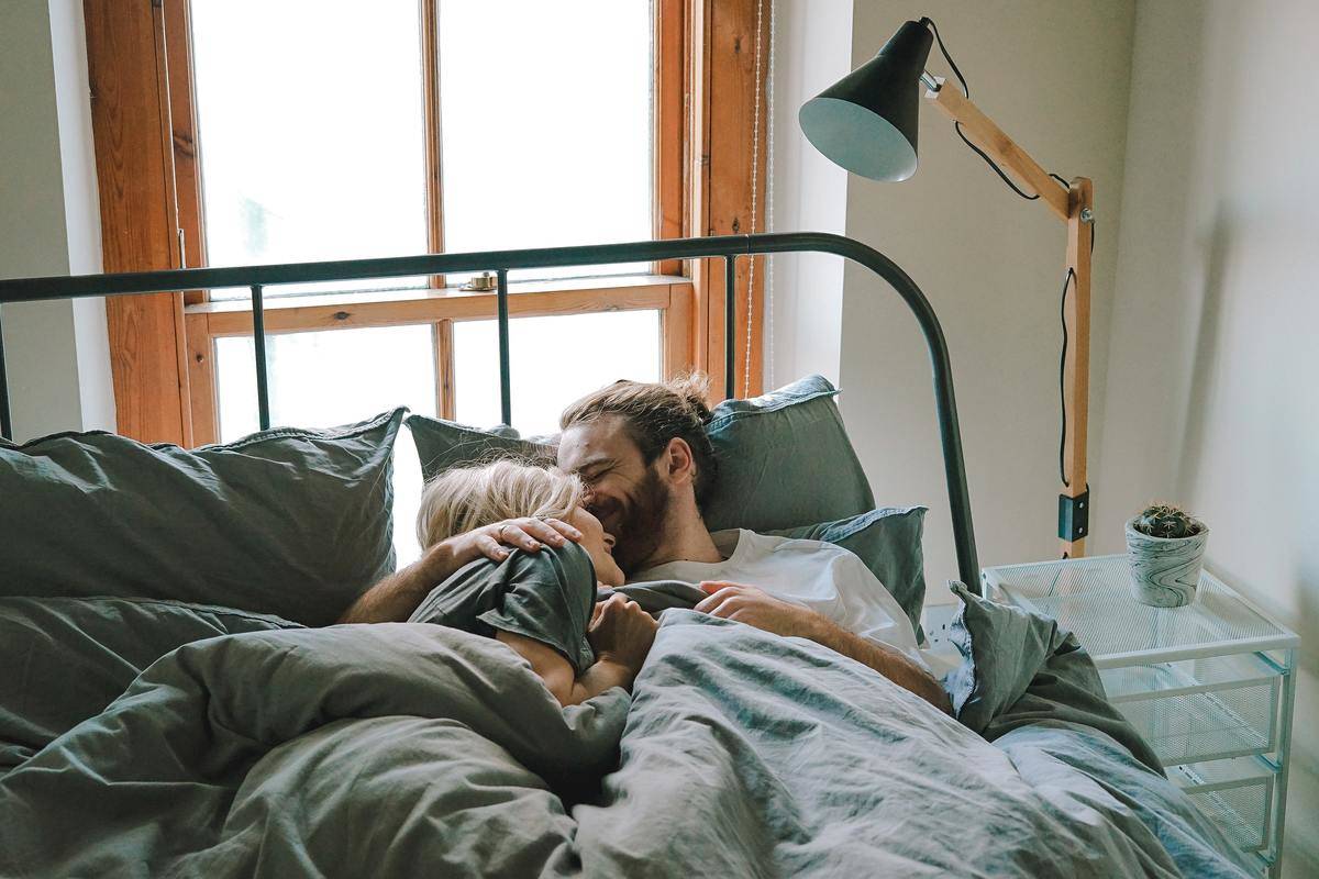 man and woman in bed cuddling and smiling under the blankets