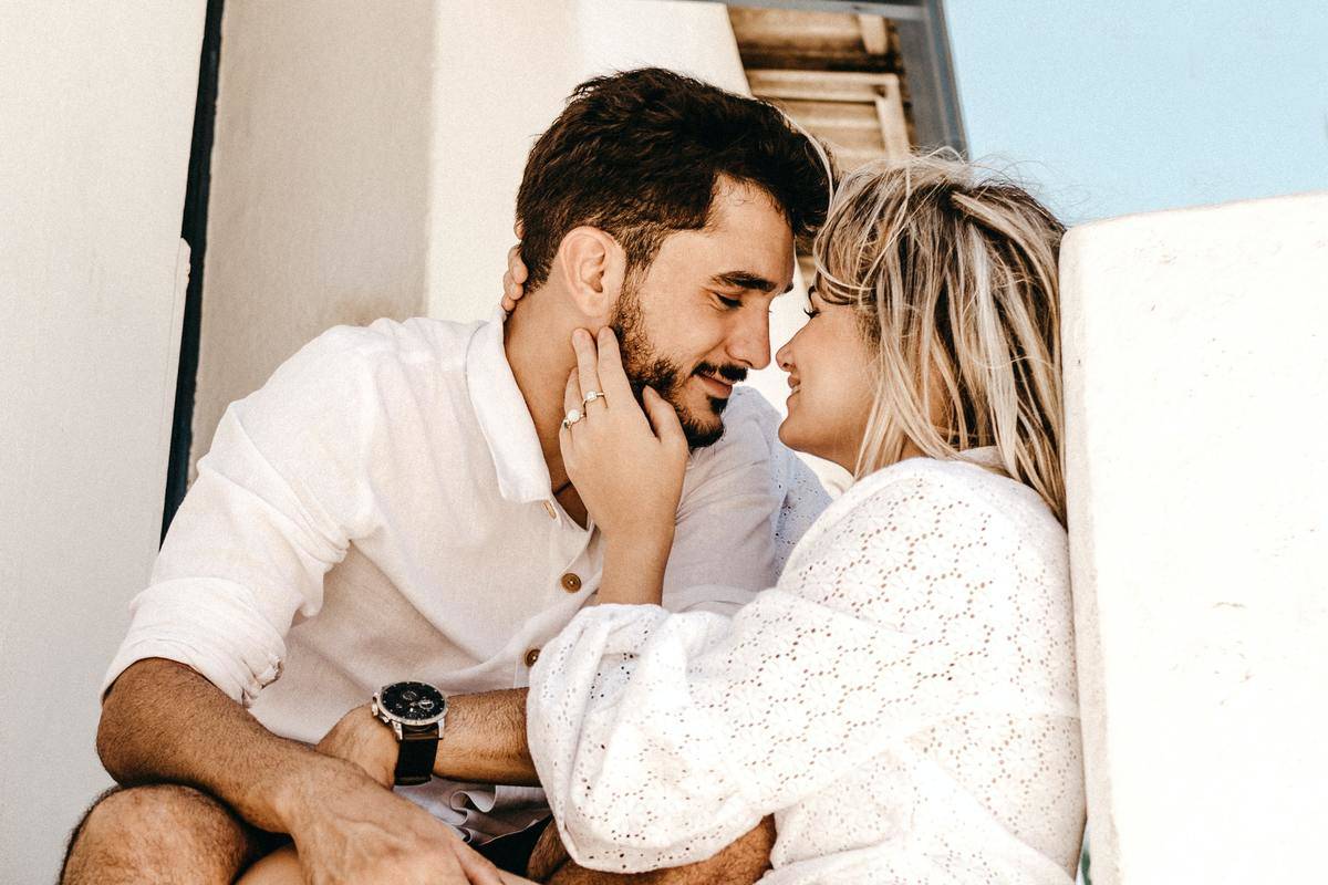 man and woman wearing white and sitting on stair case gaze into each other's eyes