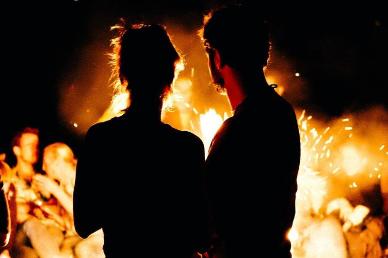 man and woman stand in front of fire looking at it