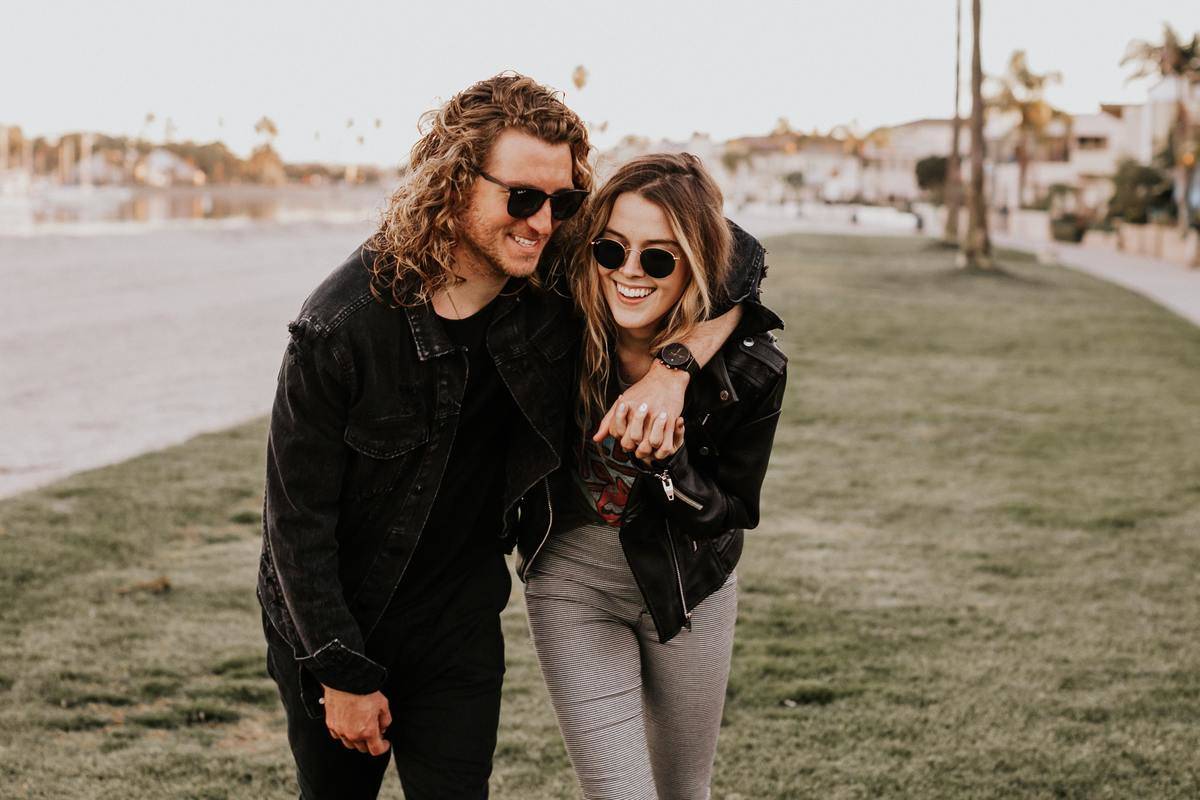 man and woman walk laughing with his arm around her, holding her hand