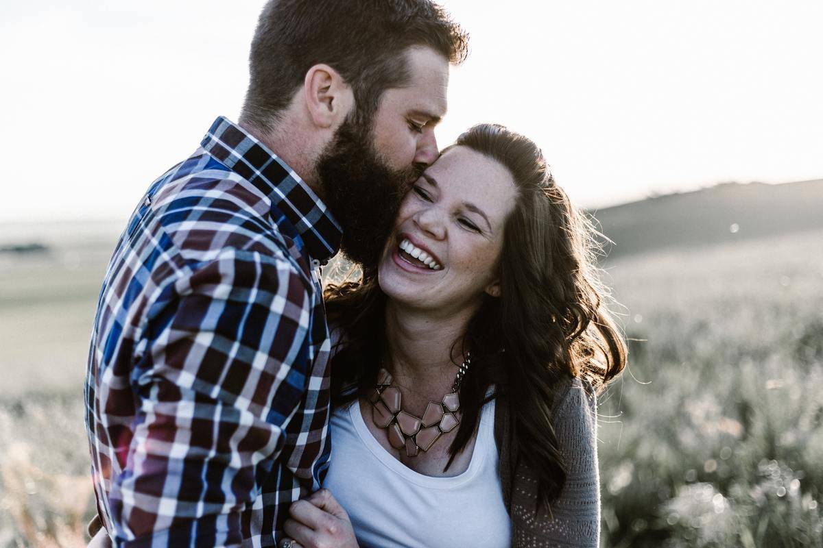 man kisses smiling woman on the cheek with eyes closed in a field